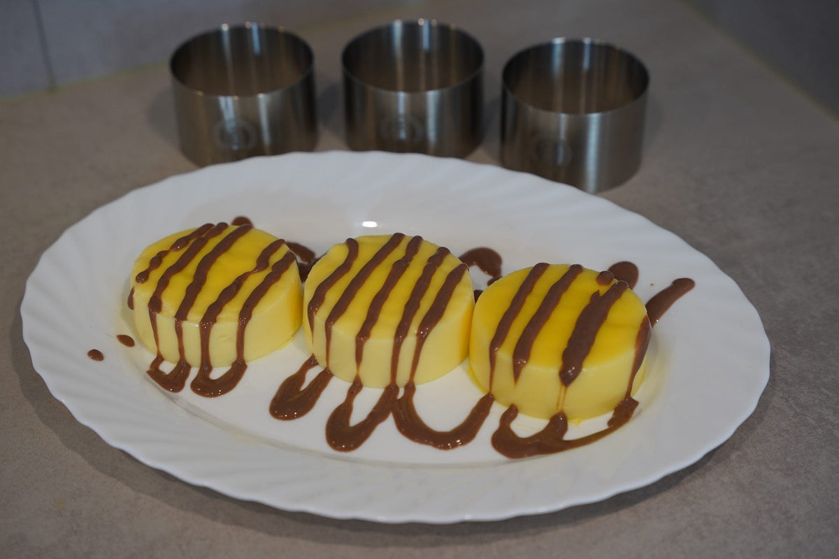 Drei Vanille-Törtchen mit Schokoladensauce, dahinter drei Speiseringe aus Edelstahl